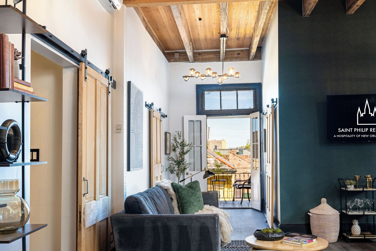 A modern interior with a wooden ceiling, a sofa, ottomans, a coffee table, and a view to the outside.