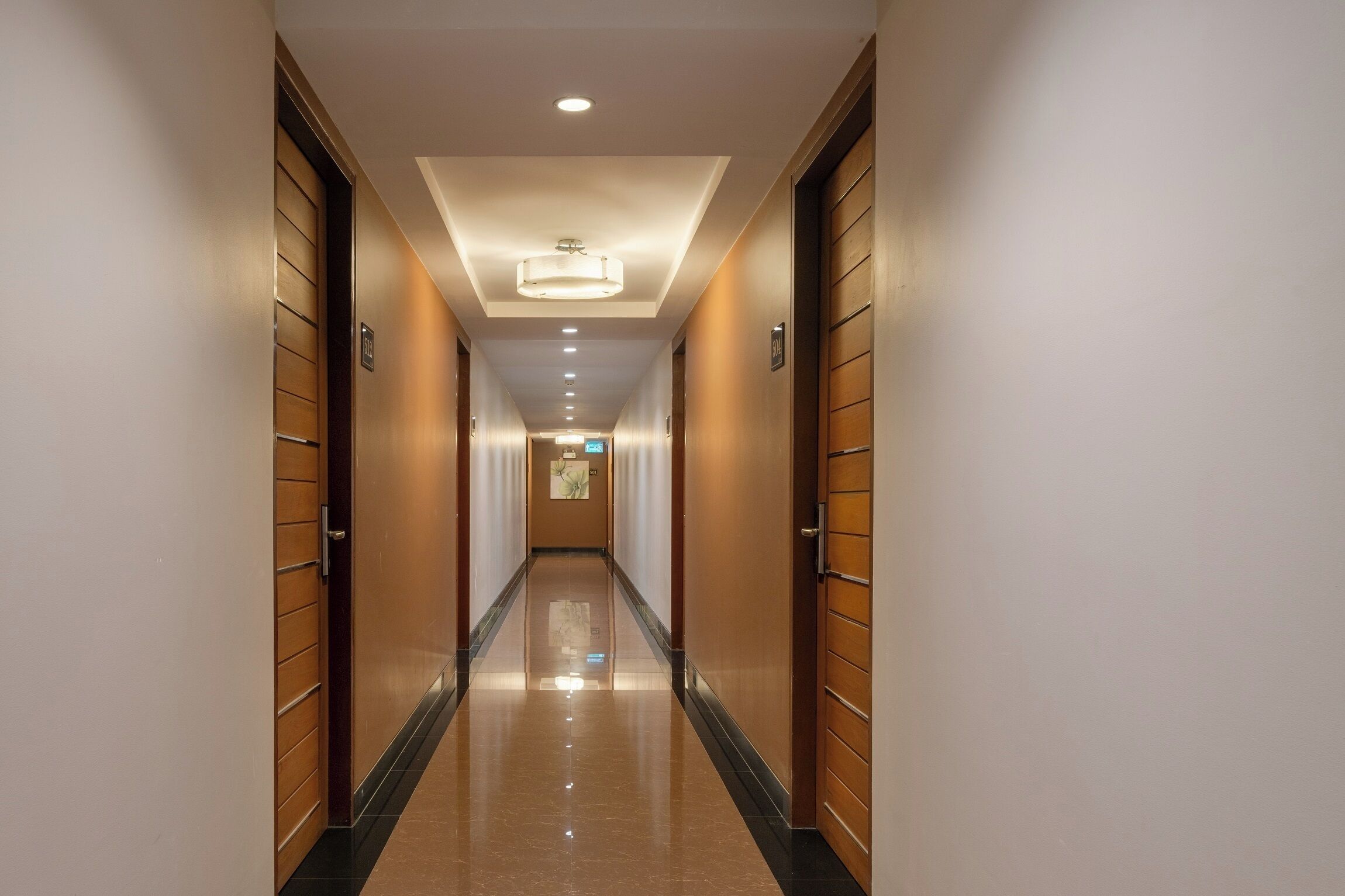 Ein langer, schmaler Hotelkorridor mit Holztüren an beiden Seiten, einem polierten Boden und eingelassener Beleuchtung in der Decke.