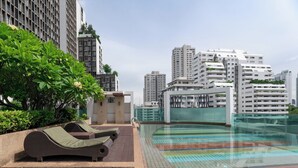 A rooftop pool area with lounge chairs, a glass-enclosed pool, and high-rise buildings in the background. - Beverly33 (Bangkok)