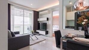 A modern living room with a sofa, a glass coffee table, and a dining area with a table set for two. - Beverly33 (Bangkok)