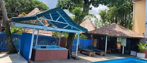 A swimming pool with a wooden deck, a hot tub, and a covered seating area.