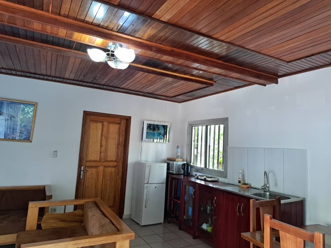 A compact kitchen with a wooden ceiling, a refrigerator, a microwave, and a sink.