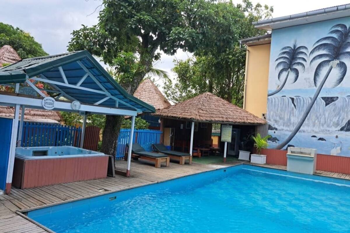 Une piscine avec une terrasse en bois, des chaises longues, un jacuzzi et une fresque représentant des palmiers.