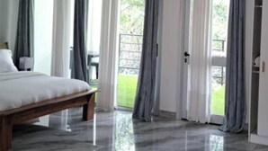 Un dormitorio con cama de madera, ropa de cama blanca y vistas a un balcón a través de amplias ventanas.