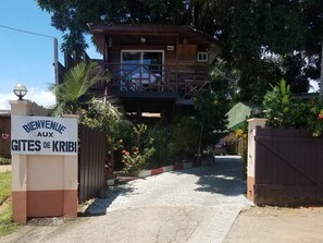 Un bâtiment en bois, avec une enseigne indiquant « BIENVENUE AUX GÎTES DE KRIBI » à l’entrée.