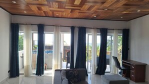 Un salón espacioso con techo de madera, ventanas grandes con cortinas, un sofá, una mesita y un escritorio.