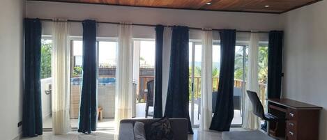Un salon spacieux avec un plafond en bois, de grandes fenêtres dotées de rideaux, un canapé, une petite table et un bureau.