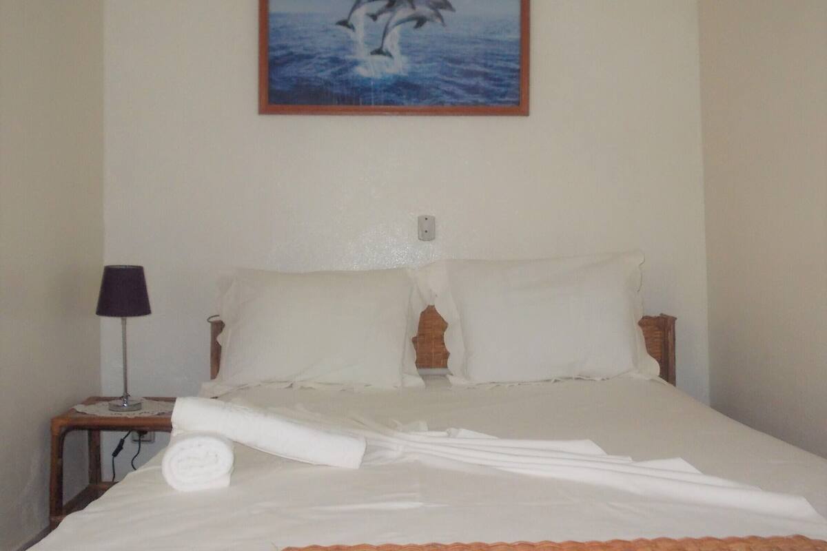 Une chambre d’hôtel avec un lit, des oreillers, une table de chevet avec une lampe et un tableau représentant des dauphins au mur.