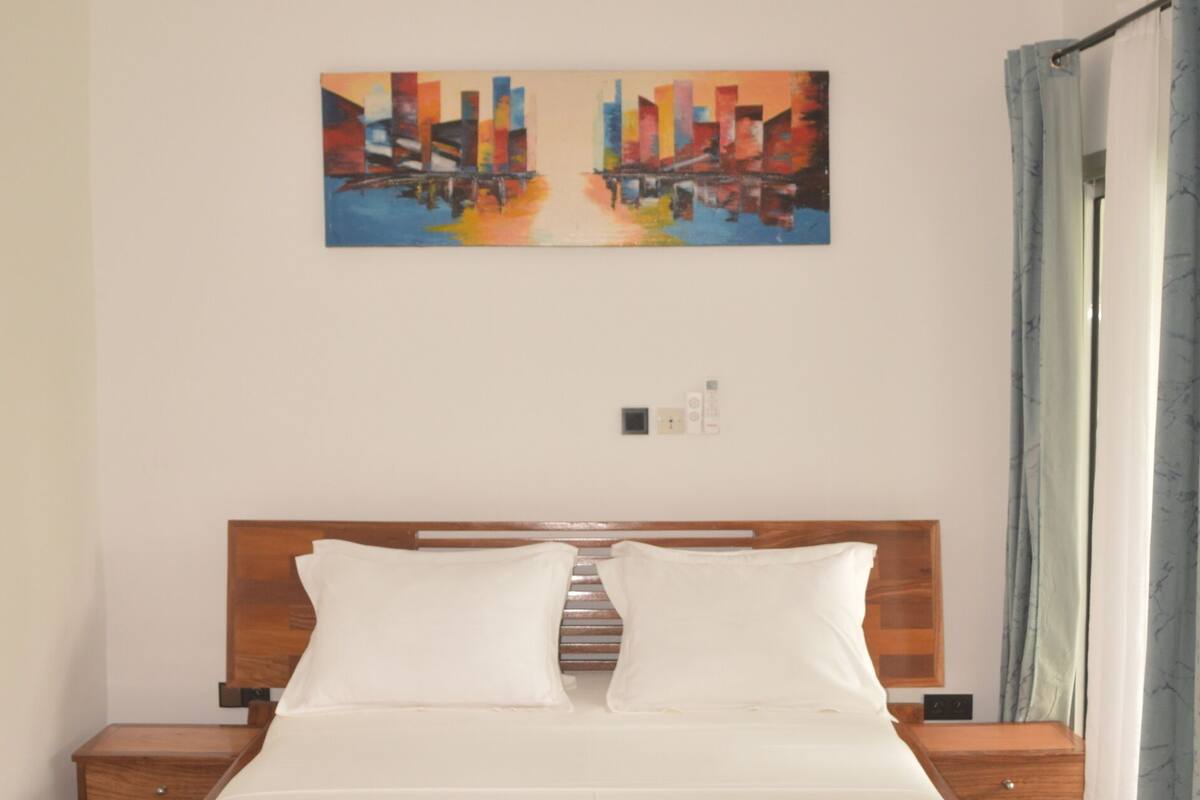 Une chambre à coucher avec un lit en bois, un ventilateur de plafond, un tableau au mur et une fenêtre avec des rideaux.