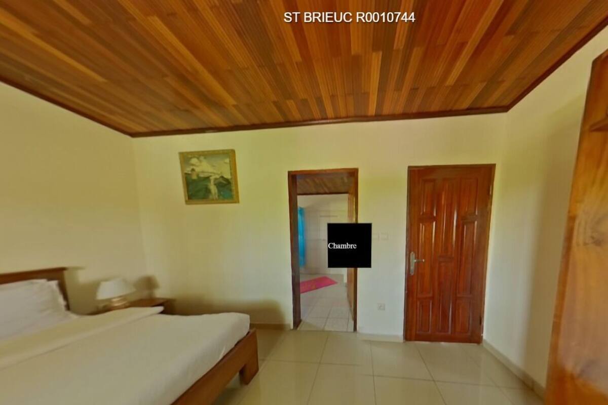 Une chambre avec un plafond en bois, un lit, un tableau accroché au mur et une porte sur laquelle est inscrit le mot « Chambre ».