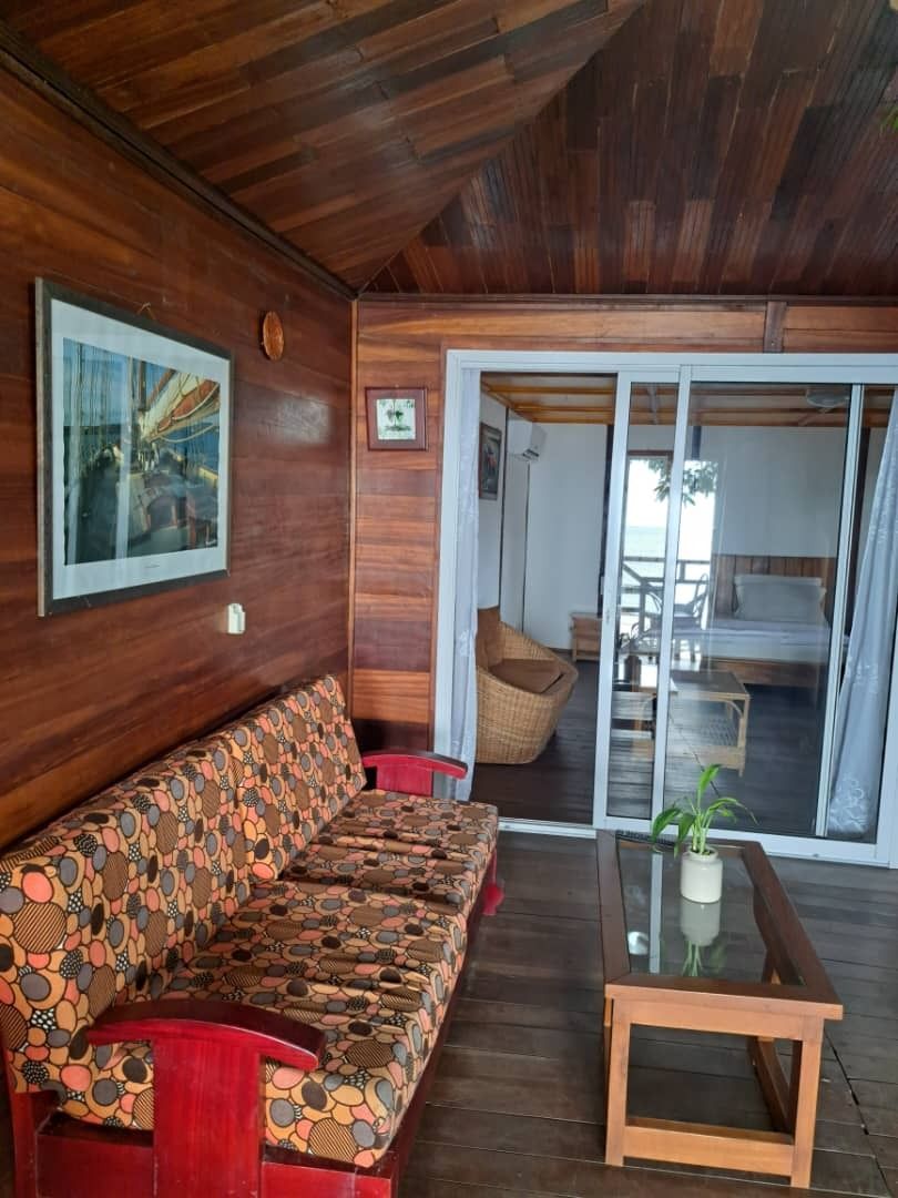 A wooden interior with a patterned sofa, a small table, and a sliding glass door leading to an outdoor area.