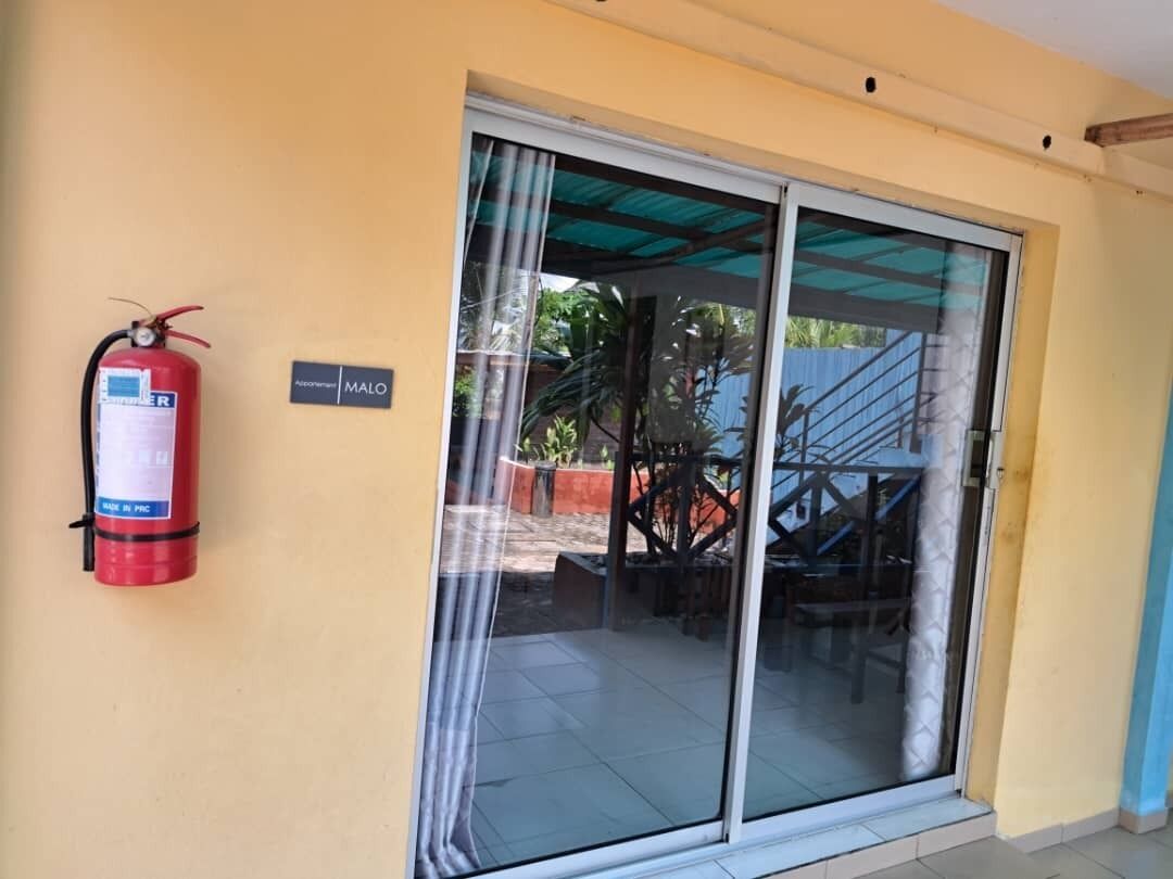 Un extintor en la pared, una puerta corrediza de vidrio y una escalera que da al exterior.