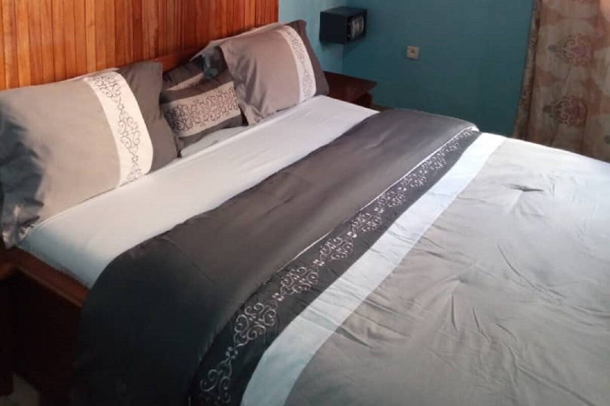 Une chambre à coucher avec une tête de lit en bois, un lit recouvert d’une literie à motifs, un appareil de climatisation et une table de chevet avec une lampe.
