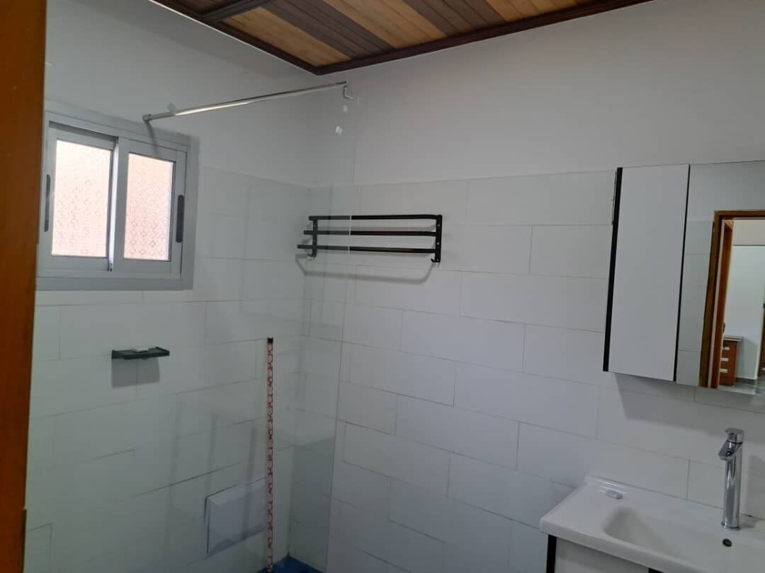 Ein Badezimmer mit weißen Fliesen, einem Fenster, einem Handtuchhalter, einem Waschbecken und einem Spiegel.