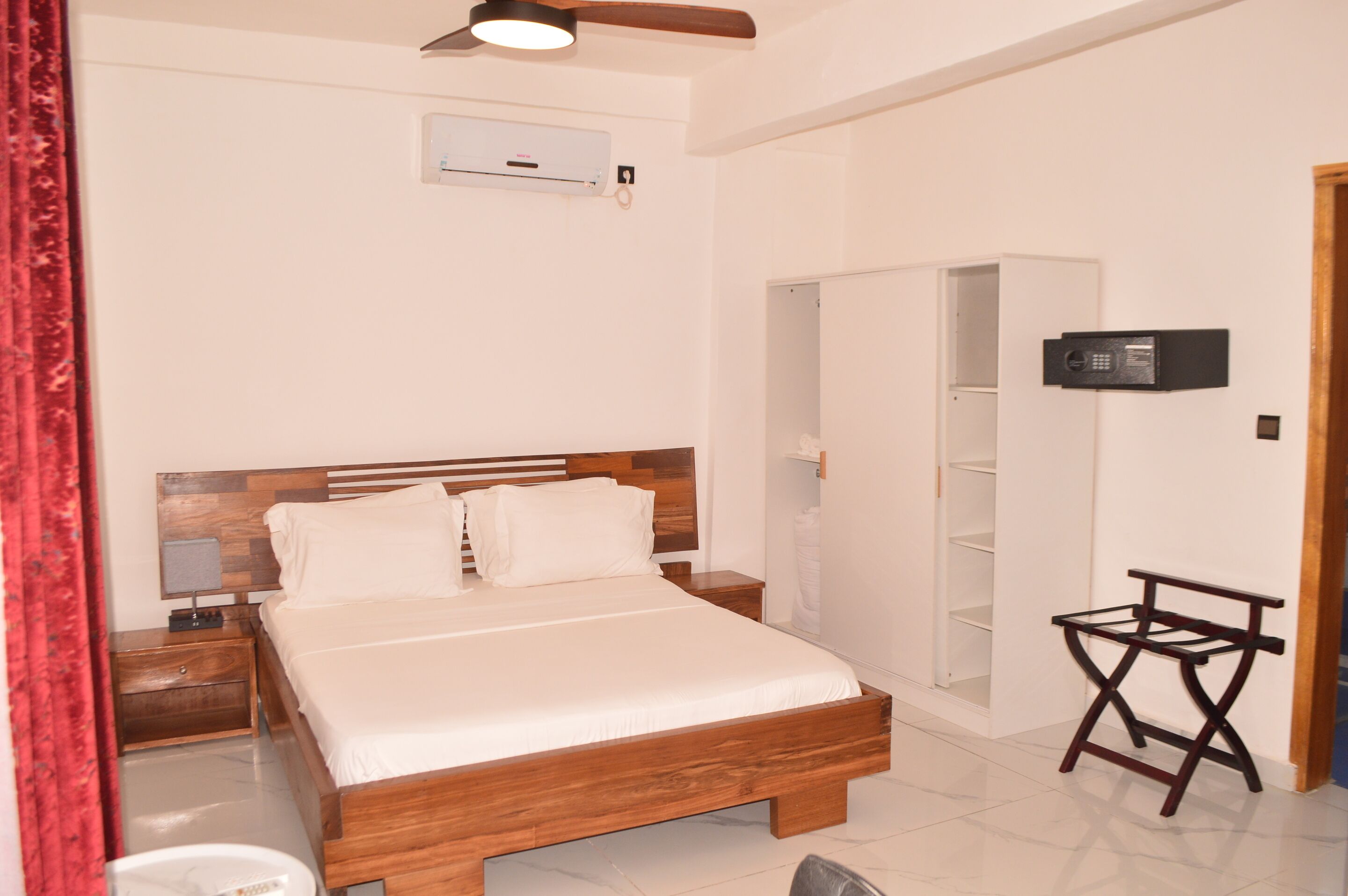 A bedroom with a wooden bed, a nightstand, a small table, a ceiling fan, an air conditioning unit, and a wardrobe.
