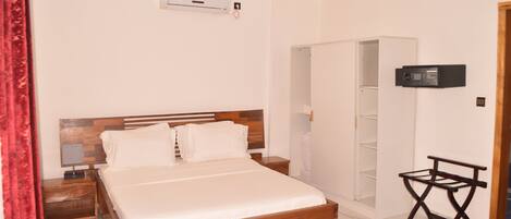 A bedroom with a wooden bed, a nightstand, a small table, a ceiling fan, an air conditioning unit, and a wardrobe.