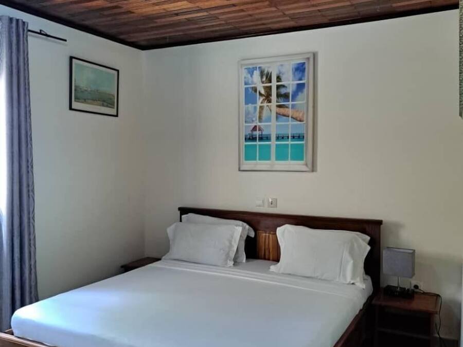 Een enkel bed met houten hoofdeinde, wit beddengoed, een nachtkastje met lamp en een lijst met afbeelding aan de muur.