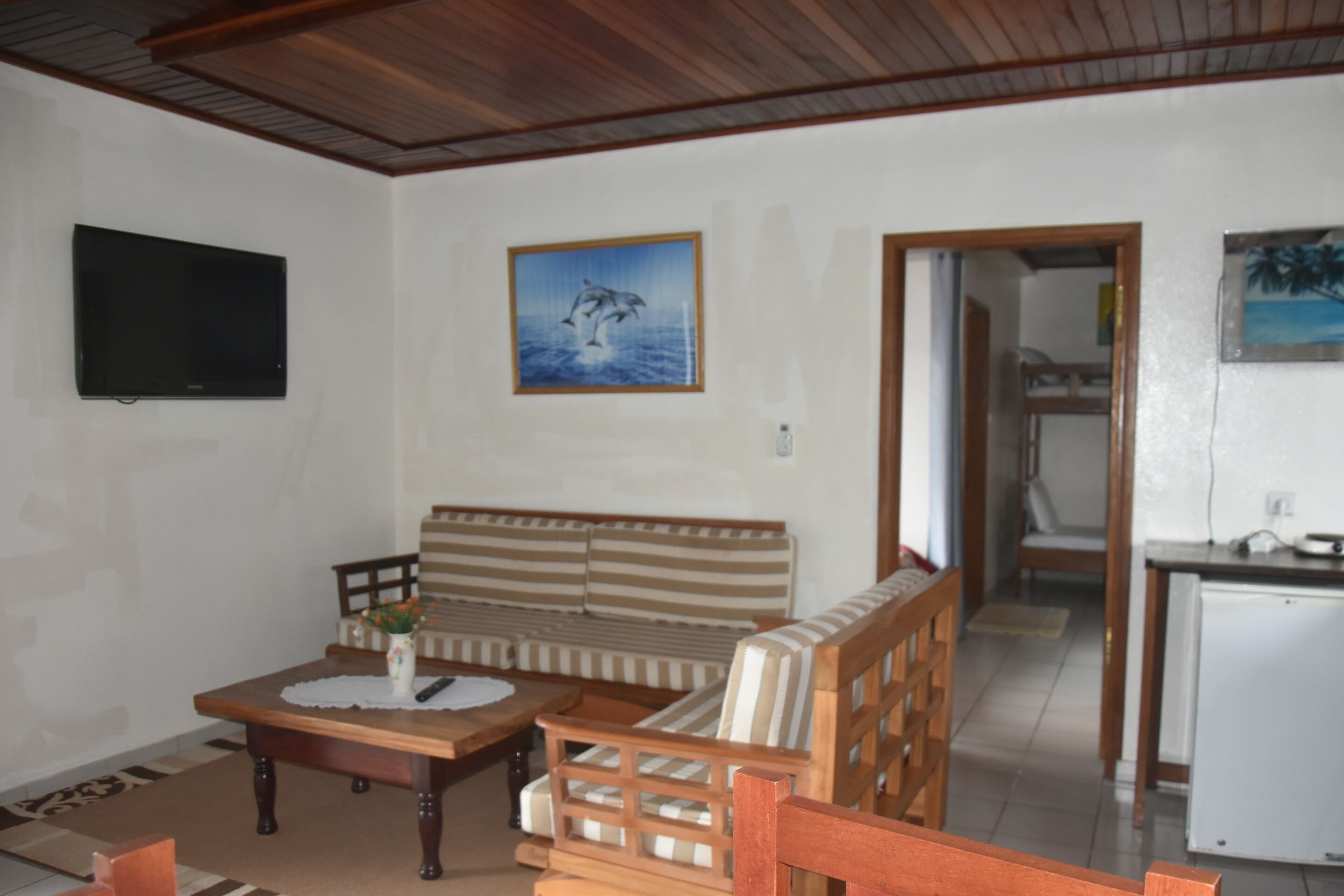 A living room with a wooden sofa, a coffee table, and a television mounted on the wall.
