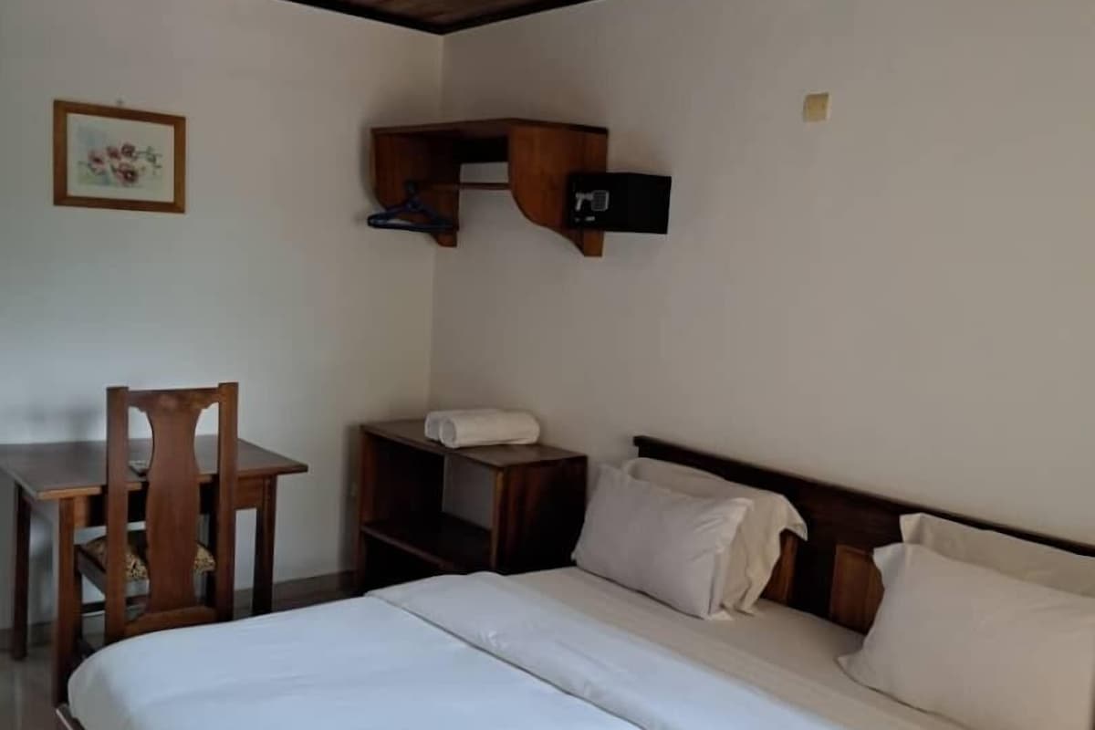 Une chambre avec un plafond en bois, un lit avec une literie blanche, un bureau en bois, une chaise et un téléviseur fixé au mur.