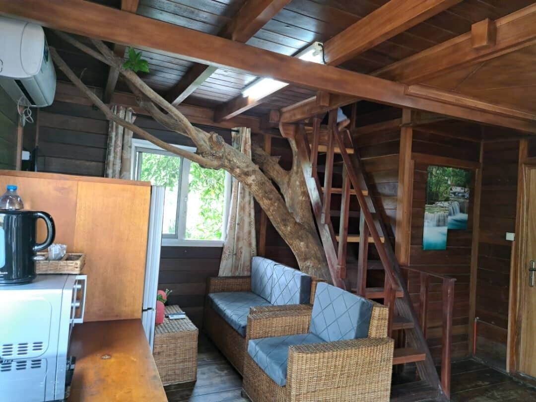 A rustic cabin interior with a wooden staircase, wicker sofa, and a coffee machine.
