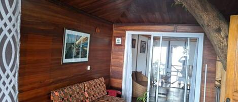 Un interior de madera con un sofá, una mesa de vidrio y una puerta que da a un balcón.