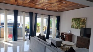 Una sala de estar moderna con techo de madera, un sofá gris, una mesita redonda y un televisor.
