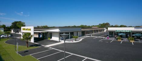 A hotel with a clear entrance, a parking lot, and a LESTAMINET store across the street.