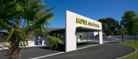 A modern motel with a clear sign reading "Motel Des Landes" and a parking area with palm trees.