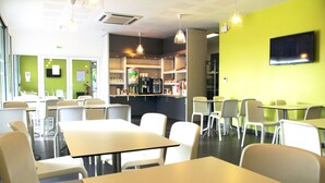Un café moderne avec des tables et des chaises blanches, un comptoir avec une machine à café et un téléviseur fixé au mur.