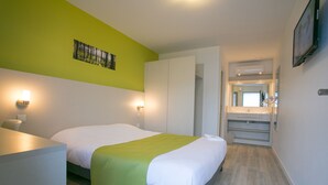 Une chambre d’hôtel moderne, équipée d’un lit, de lampes de chevet, d’un mur d’accent vert, d’une salle de bain avec un miroir et d’un téléviseur fixé au mur.