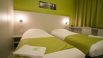 A hotel room with two beds, green bedding, a painting on the wall, and a desk with a chair.