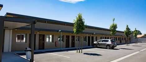A motel with a covered parking area, a row of rooms, and a car parked in the lot.