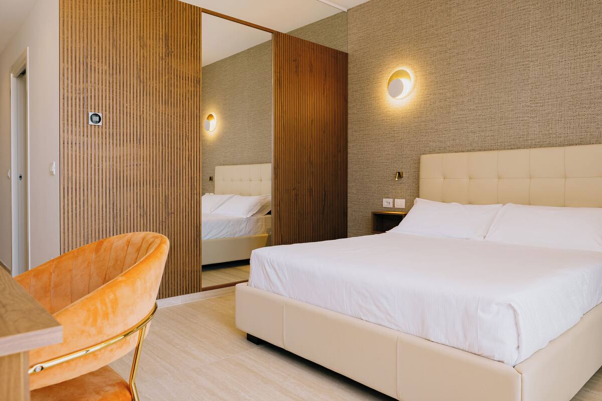Une chambre d’hôtel moderne avec un grand lit, un mur lambrissé en bois, un miroir et un applique murale ronde.