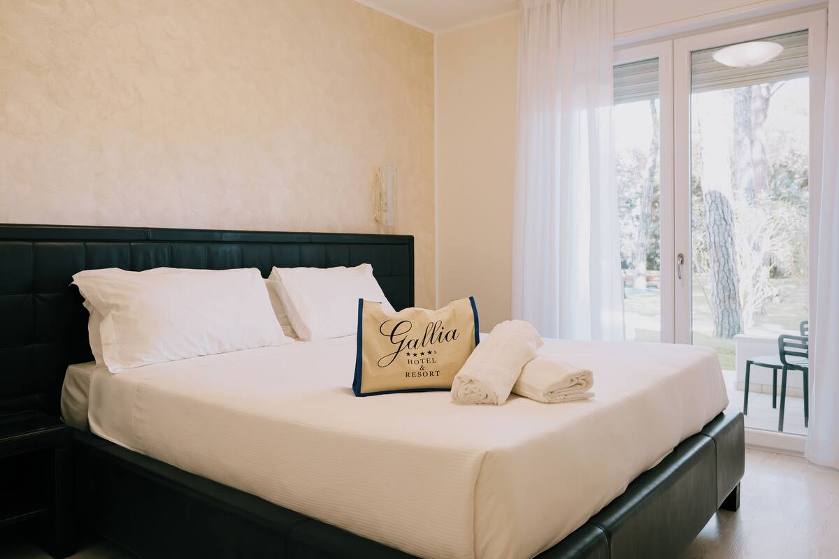 Un lit bien fait, avec du linge de lit blanc, un oreiller orné du texte « Gallia Hotel Resort » et une serviette enroulée.