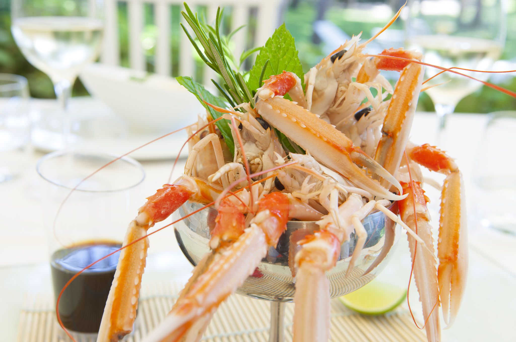 A bowl of cooked lobster with a garnish of herbs, accompanied by a glass of sauce and a lime wedge on a table.
