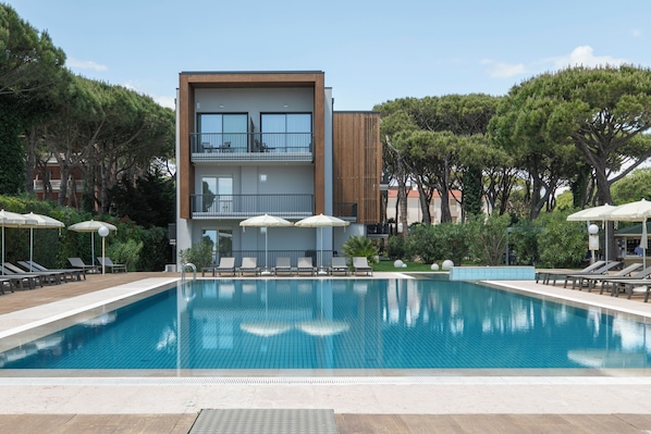 A modern building with a pool, lounge chairs, and umbrellas. - Hotel & Resort Gallia (Jesolo)