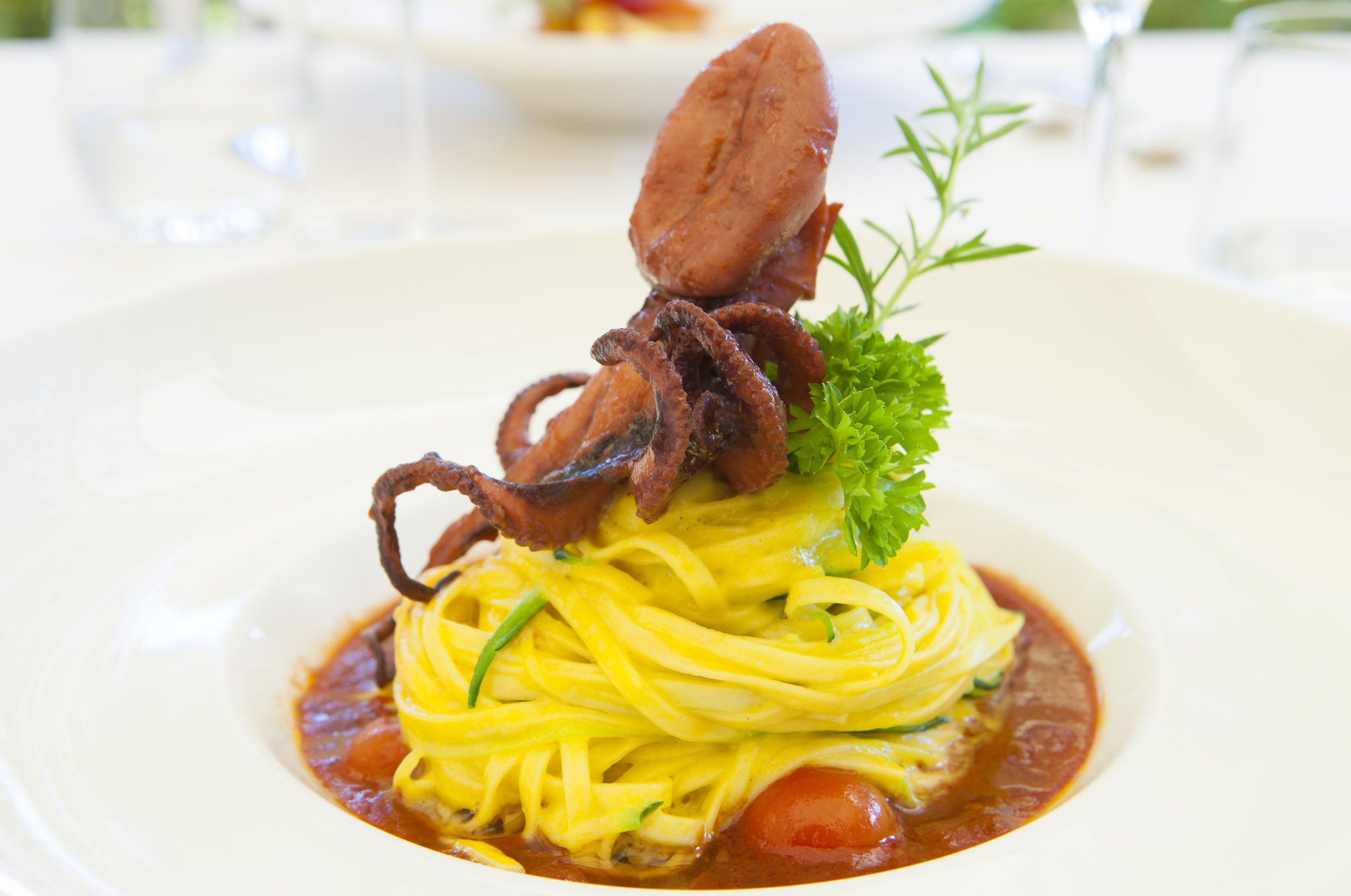 A plate of spaghetti with a tomato-based sauce, garnished with parsley and a piece of meat.