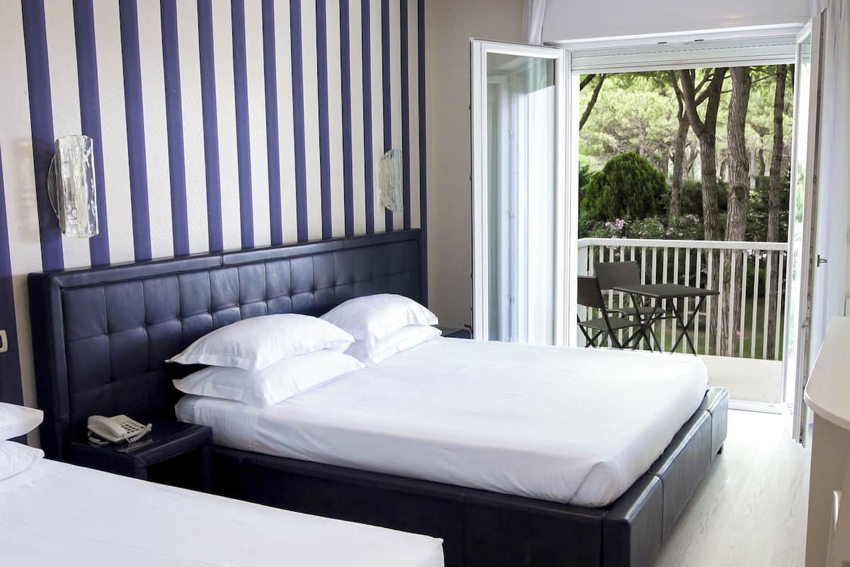Une chambre d’hôtel avec un grand lit, une table de chevet avec un téléphone et une vue sur un balcon équipé d’une chaise.