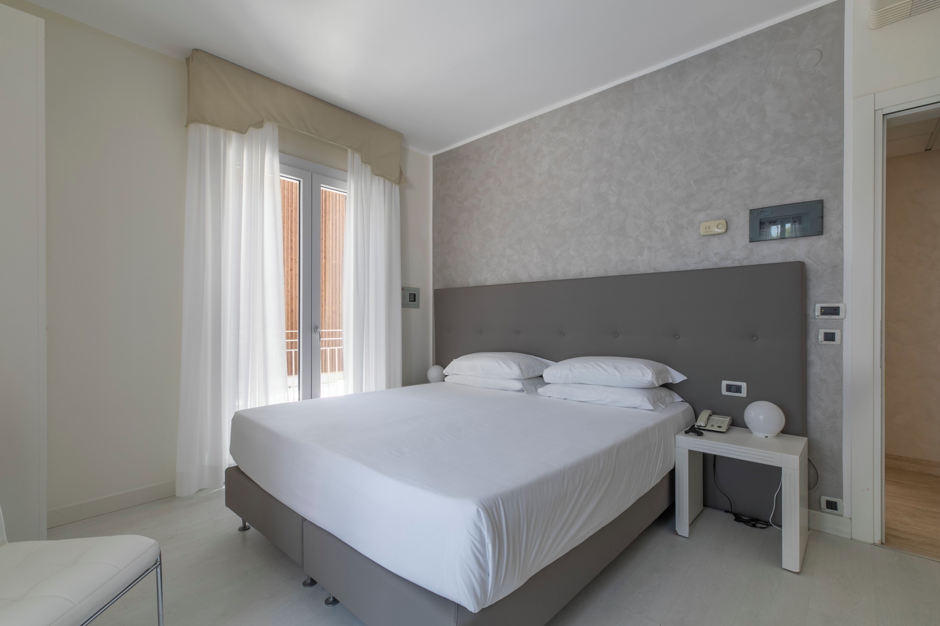 Une chambre moderne avec un grand lit, une table de chevet avec une lampe et une fenêtre avec des rideaux.