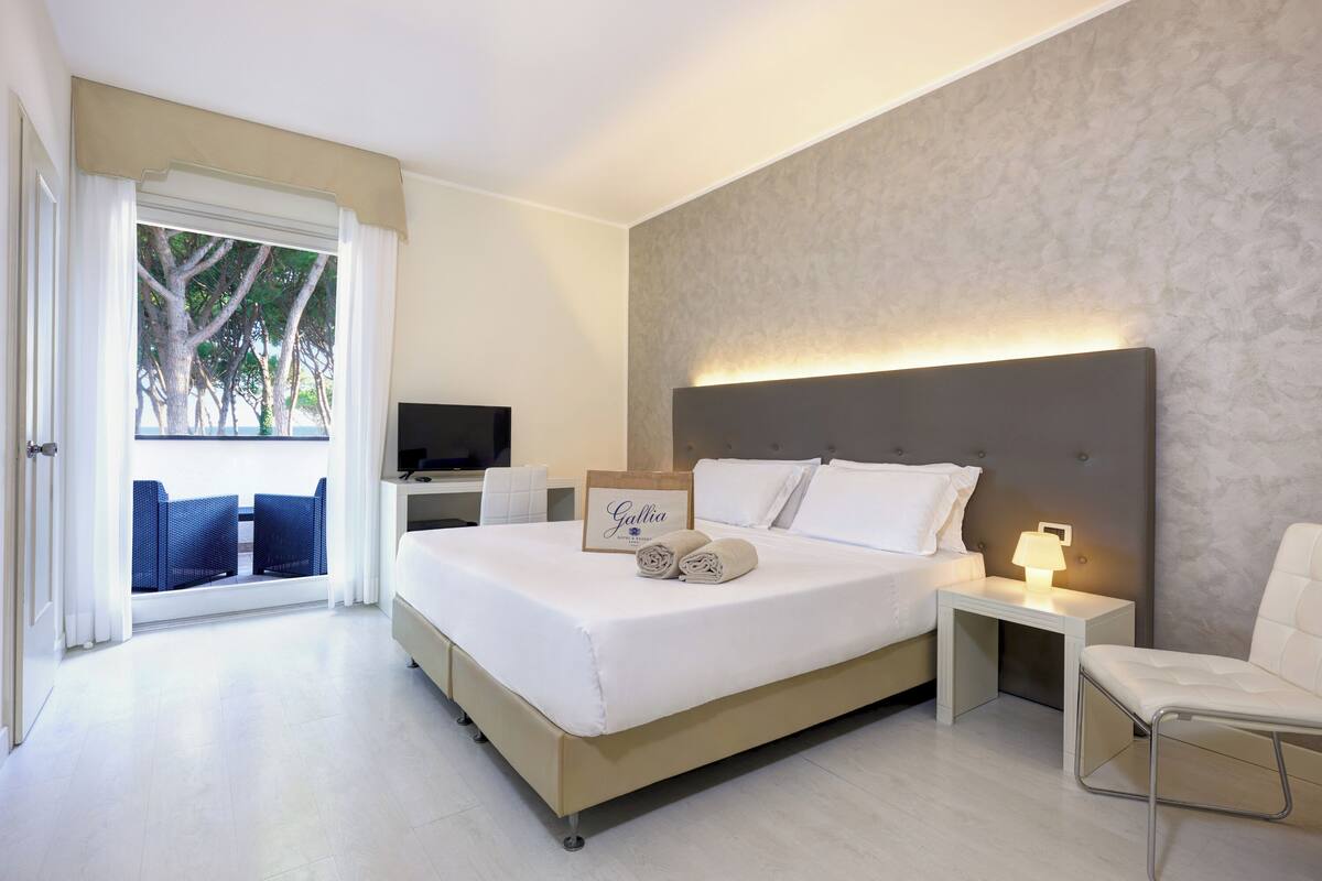 Une chambre d’hôtel moderne dotée d’un grand lit, d ’une table de chevet avec une lampe, d’une télévision et offrant une vue sur l’extérieur grâce à une grande fenêtre.