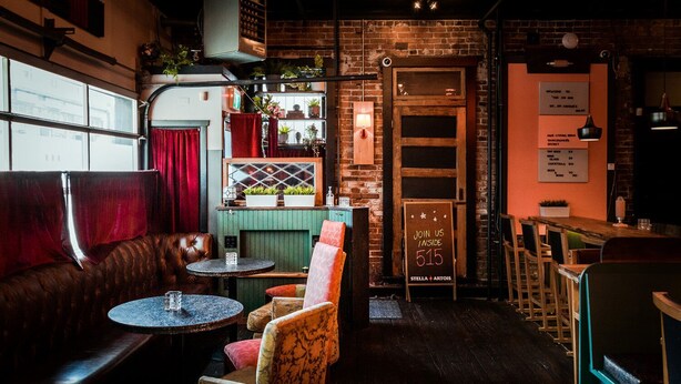 A cozy bar area with leather seating, a brick wall, and a sign inviting guests to join inside. - Cambie Downtown Hostel (Vancouver)