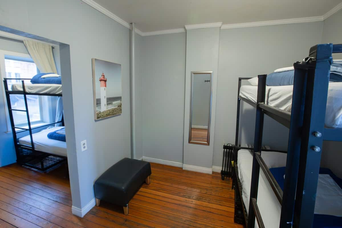 Une pièce avec des lits superposés, un banc, un miroir et un tableau encadré au mur.