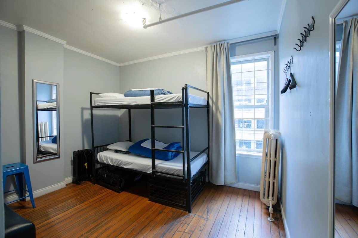 Une chambre avec un lit superposé, une fenêtre, un radiateur et un miroir au mur.
