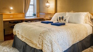 A neatly made bed with a textured blanket and pillows, a desk with a lamp, and a window with curtains. - Cambie Downtown Hostel (Vancouver)