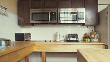 A kitchen with two stainless steel microwaves, a toaster, and a kettle on the counter.