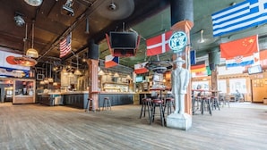 Amplia zona de bar con varios taburetes, una estatua y banderas de diferentes países.
