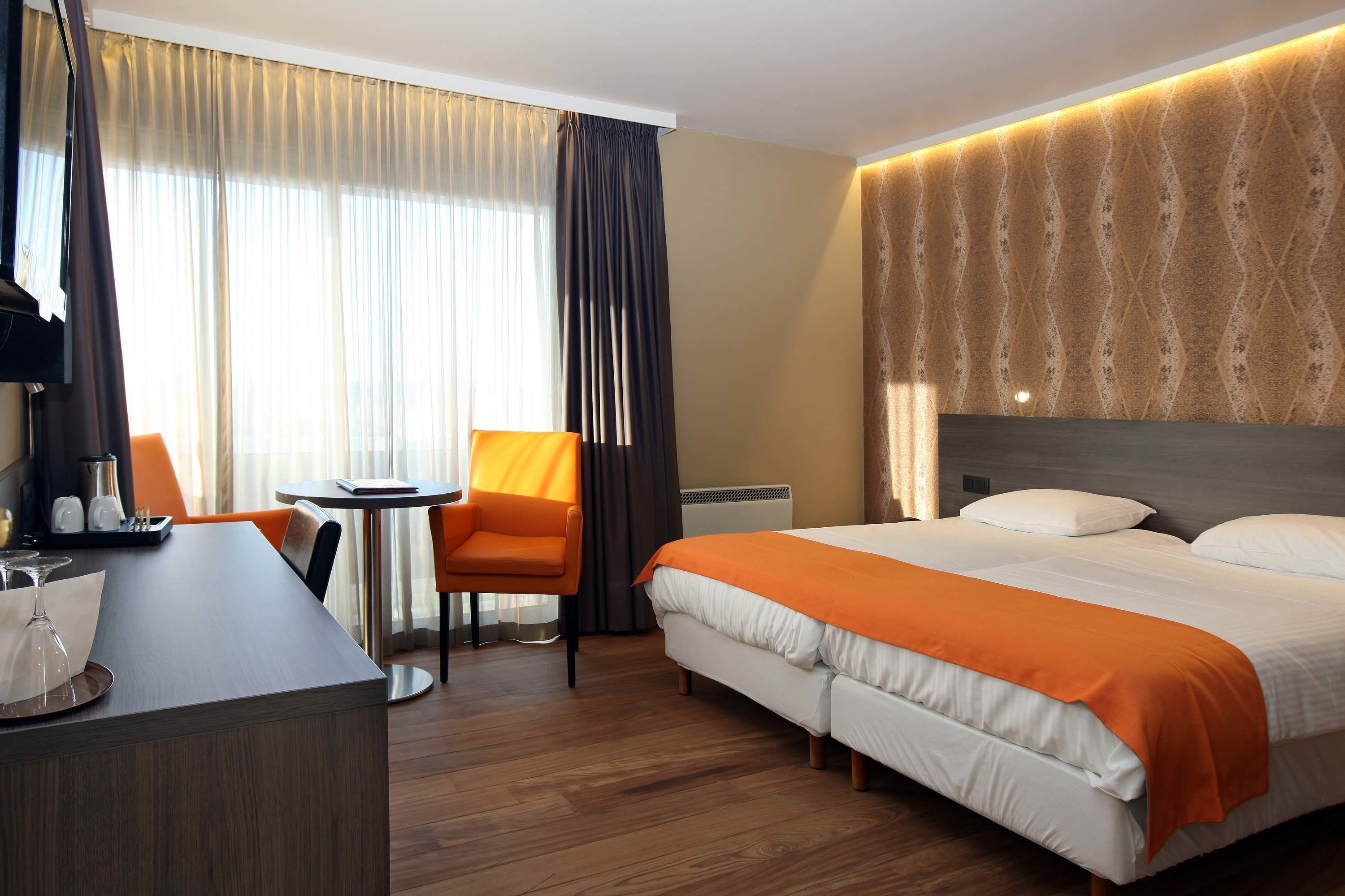 A hotel room with a bed, a desk, a chair, and a small table.