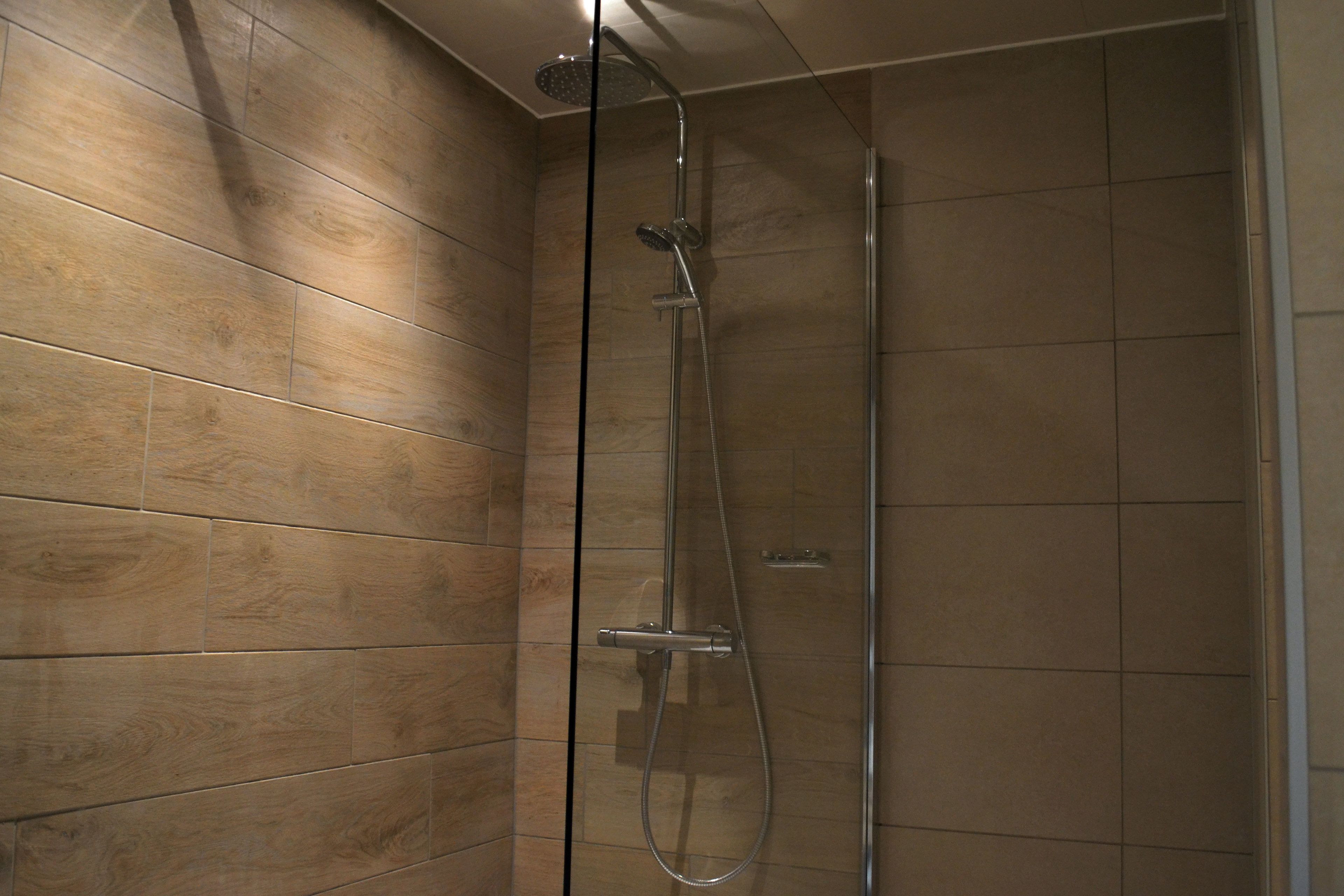 A shower with a glass door and wooden panel walls.