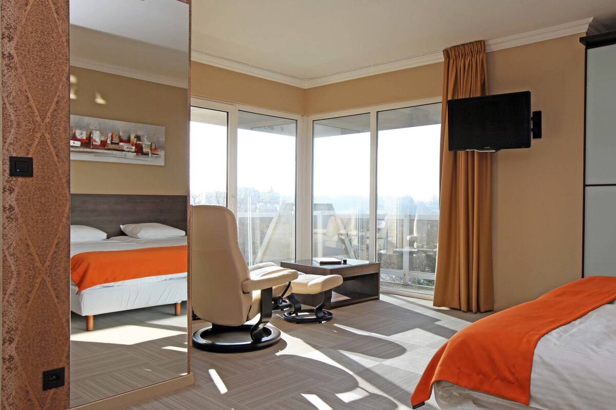 A hotel room with a bed, a chair, a desk, a TV, and a large window with a view.