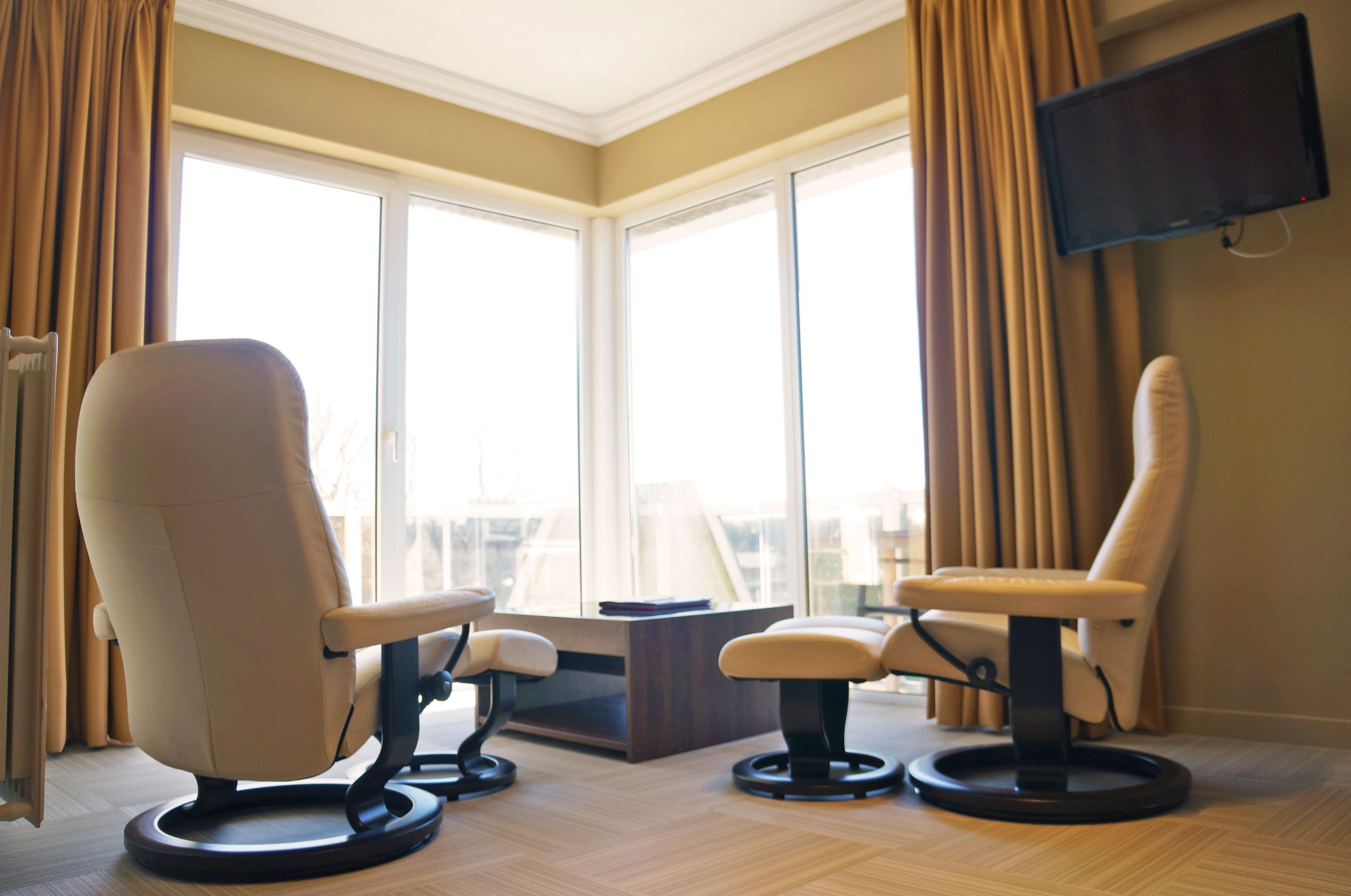 A modern room with two leather chairs, a small table, and a TV mounted on the wall.